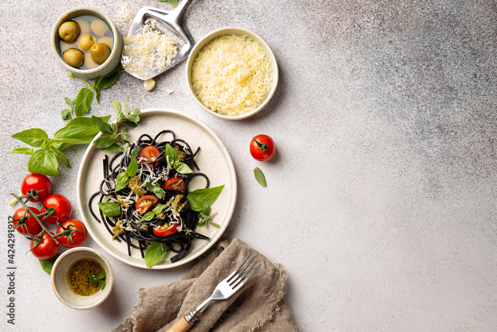 Black spaghetti with dried tomatoes,parmesan cheese,pesto,basil and fresh marjoram and different dishes for italian pasta.Top view,flat lay. Black spaghetti with dried tomatoes,parmesan cheese,pesto,basil and fresh marjoram and different dishes for italian pasta.Top view,flat lay.