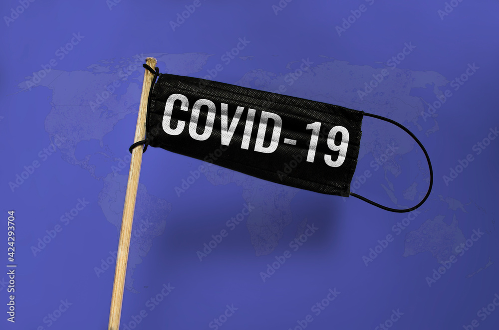 Fototapeta premium The medical mask Waving black flag on pole with text COVID-19. Black mask on blue the world map textured background. Black virus Attack flag. Concept of coronavirus COVID