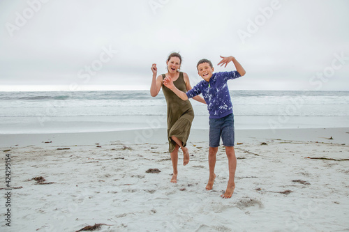 Happy playful family have fun on the beach. Young mother and son run and jump at sunset on ocean coastline.
