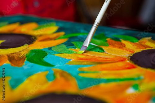  A hand with brush drawing picture of sunflowers by acrylic paints on canvas. Art concept.