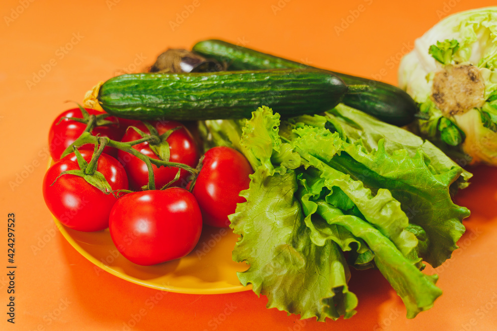 Close up of appetizing tomatoes, cucumbers, lettuce and cabbage on orange background. Harvest of ripe vegetables for healthy nutrition. Concept of organic products and eco-friendly lifestyle.