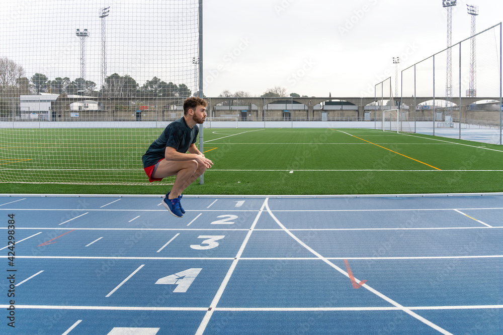 Fototapeta premium Hard working young runner boy doing warm-up in blue running track.