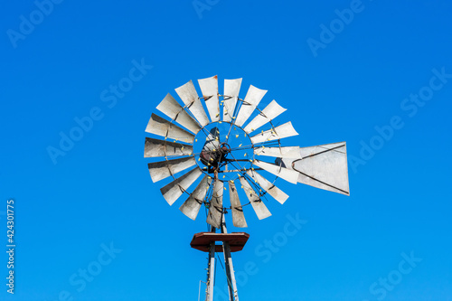 Classic vintage multi bladed wind pump, bladed rotor decorated with string lights against blue sky.