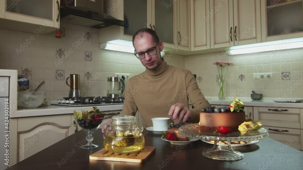 Man in glasses drinks coffee and eats cake at kitchen Man in glasses drinks coffee and eats cake at kitchen
