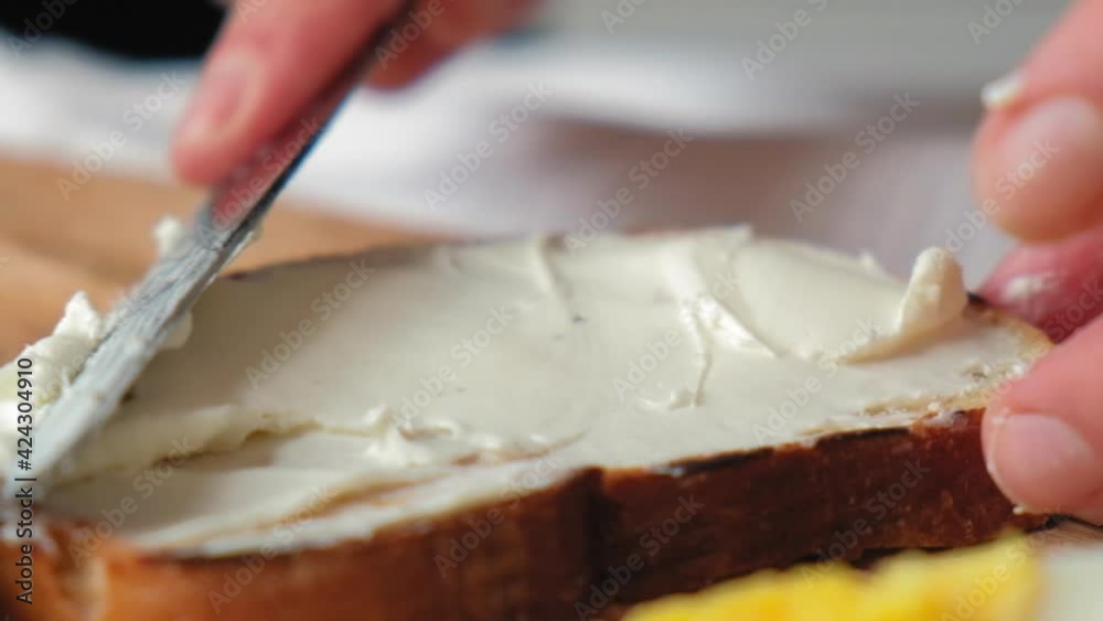A chef in a bright kitchen spreads soft Philadelphia cheese on toasted toast. Women's hands in a bright kitchen are spreading soft cheese and butter on toasted toast. Close-up in slow motion, colorful A chef in a bright kitchen spreads soft Philadelphia cheese on toasted toast. Women's hands in a bright kitchen are spreading soft cheese and butter on toasted toast. Close-up in slow motion, colorful