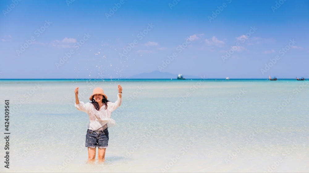 Young woman traveler walking down to the sea on the white sand beach and blue sky of islands in the Andaman Sea of Thailand.Suitable for summer travel and leisure. Young woman traveler walking down to the sea on the white sand beach and blue sky of islands in the Andaman Sea of Thailand.Suitable for summer travel and leisure.