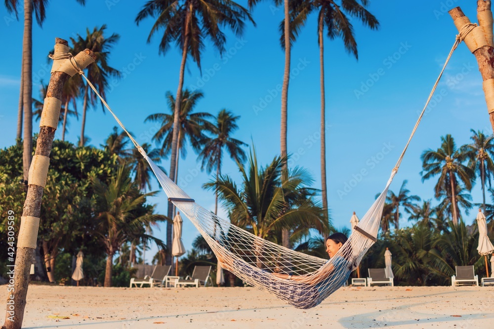 Obraz premium Asian traveler woman lying on the hammock on the beach in tropical resort hotel with Coconut tree and blue sky background.Travel in weekend holidays concept.