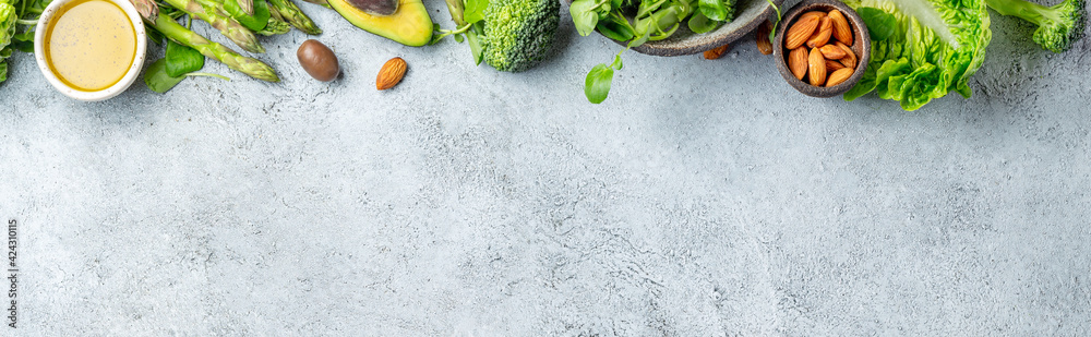 Fototapeta premium Vegetarian green ingredients on gray background. Vegetarian food - vegetables, greens, avocado, oil - health or cooking concept. Background layout with free text space