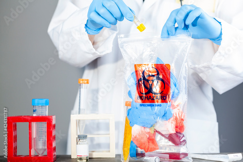 A woman researcher is holding a clear plastic bag with biohazard logo printed on. The bag contains, potentially dangerous biological specimens. Scientists discard these waste in these labelled bags. photo