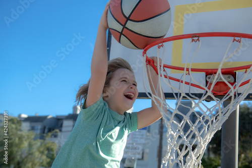 Close up image of basketball excited kid player dunking the ball, outdoor on playground. Child scoring slam dunk, stock photo.