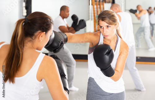 Young focused woman practicing boxing punches in sparring during group self defence course in gym © JackF