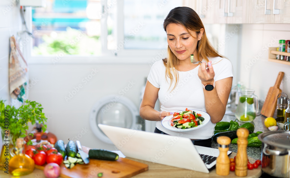 Woman cook reads the recipe in laptop and cooks soup in the kitchen