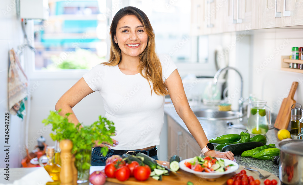 Young colombian housewoman cooking vegetable salad at home kitchen