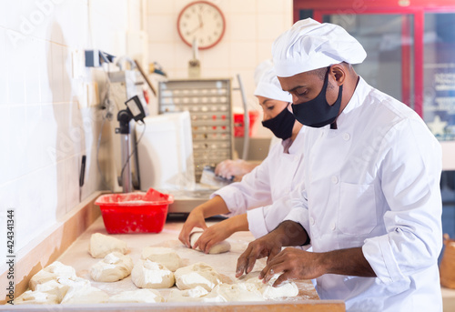 Male and female baker in protective mask working together in bakery shop