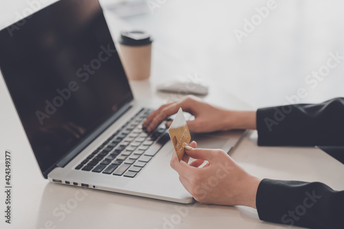 Close up of a business woman hand holding a credit card shopping online using laptop at the office.
