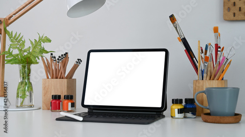 Mock up computer tablet, coffee cup, stylus pen and painting tools at artist or creative designer workplace.