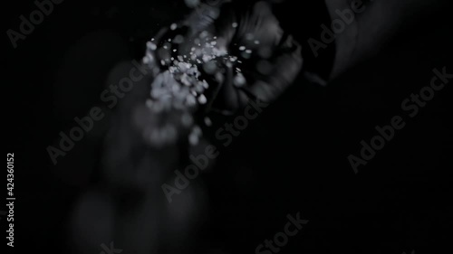 Person sprinkling salt. Chef sprinkles salt crystals over camera. black background, slow motion, close up