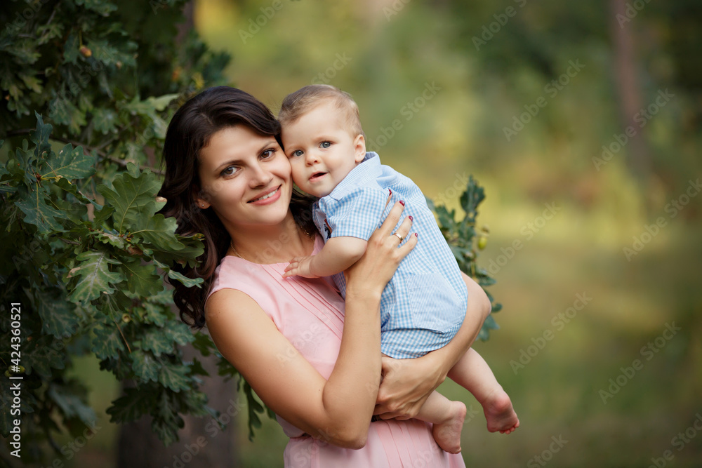 Happy family in a summer park. Family day. Little Boy with his mom in casual green outfit. Sunny summer day outdoors. Mother is holding her little son in hands. Walk in nature forest