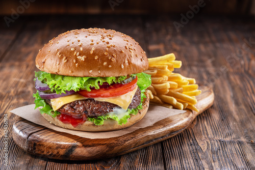 Delicious burger with  potato fries on a wooden table with a dark brown background behind. Fast food concept.