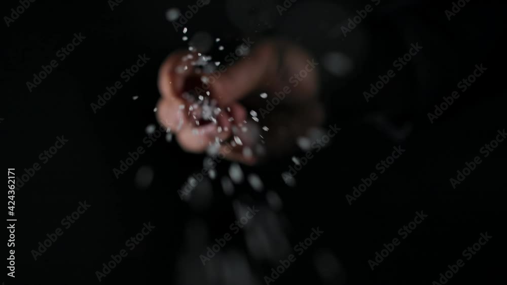 Person sprinkling salt. Chef sprinkles salt crystals over camera. black background, slow motion, close up