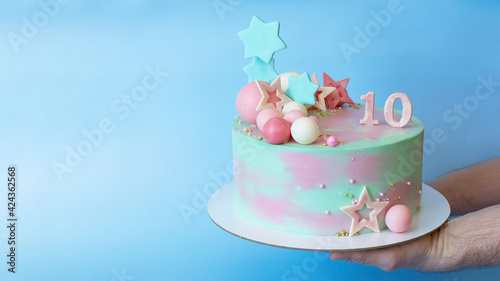 
A beautiful birthday cake decorated with chocolate balls and pink and blue stars. With number 10, on a blue background. Place for an inscription.