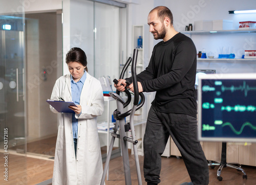 Sport researcher in laboratory taking notes while muscular athlete athlete is running, heart rate examination. Testing endurance in professional biomechanics lab. photo