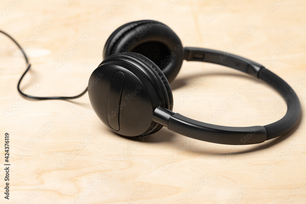 Black headphones with wire on wooden background Black headphones with wire on wooden background