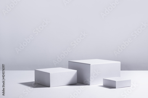White square podiums in sunlight with shadow in white space. Showcase for cosmetic products, goods, shoes, bags, watches.