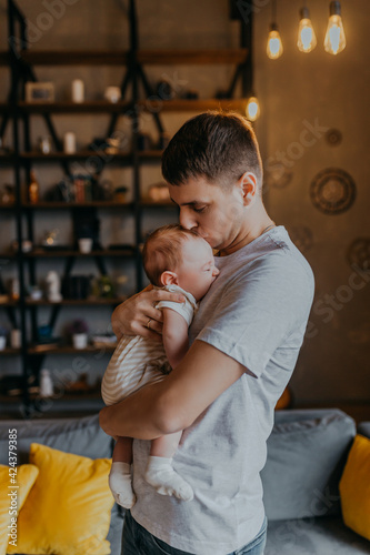 Father holds little crying baby in arms. Dad kisses son. Father sitting with a kid alone.
