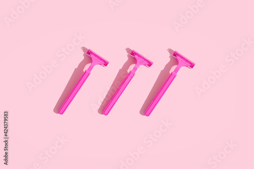 Minimal feminine's body care concept: three female raspberry shavers with hard shadows on a pink background. 