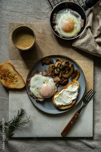 Breakfast with fried egg(sunny side up) with bacon, grilled with rosemary mushrooms and toast with cream cheese. 