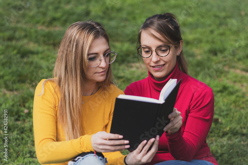 Two women enjoying reading a book in a park