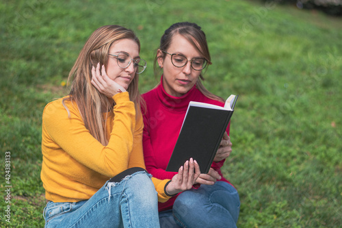 Two women enjoying reading a book in a park