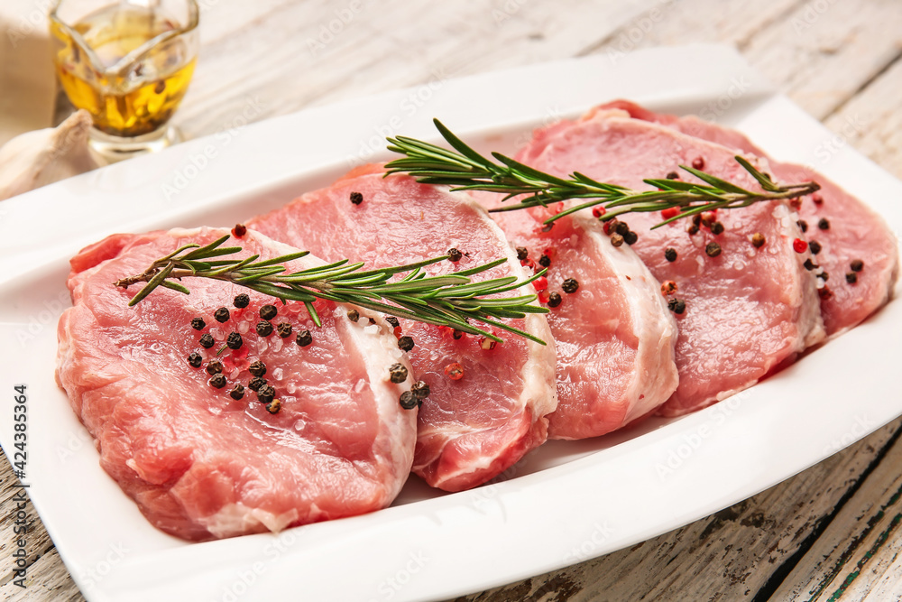 Plate with fresh raw meat and spices on wooden background