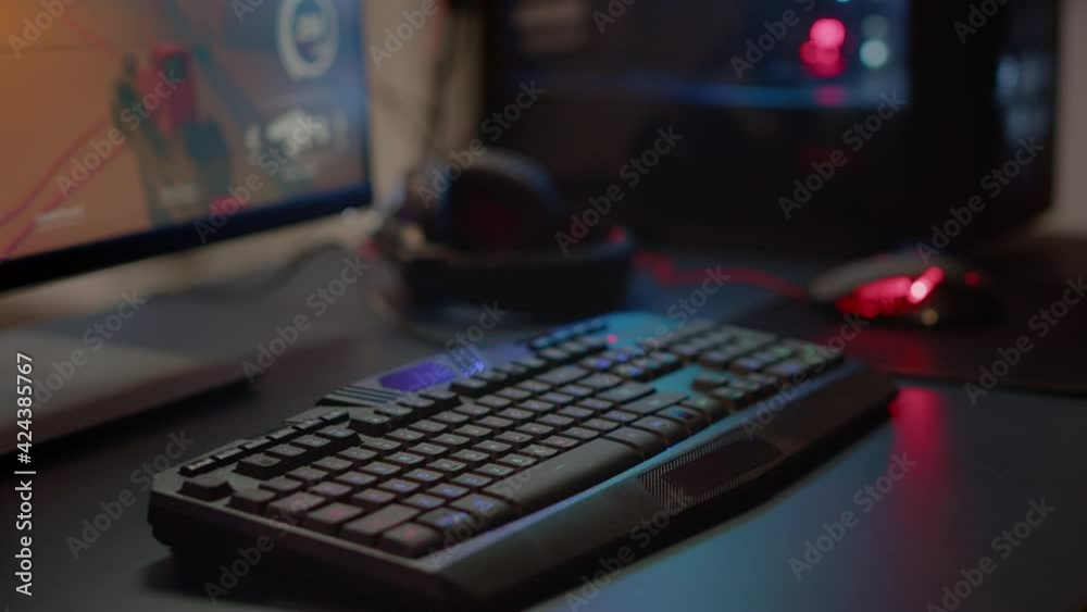Close up of professional RGB keypad in empty gaming room prepared for streaming online tournament, display with first person shooter playing on it. Game studio with powerful computer Close up of professional RGB keypad in empty gaming room prepared for streaming online tournament, display with first person shooter playing on it. Game studio with powerful computer
