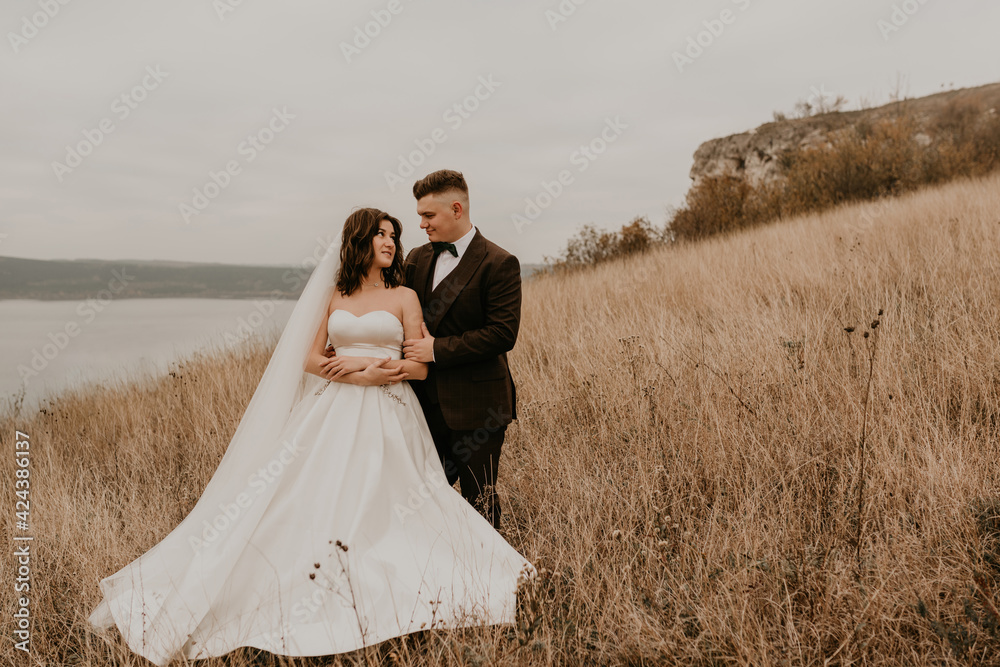 couple wedding newlyweds in walk hug kissing on tall grass on mountain above the river