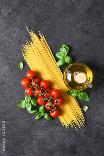 Spaghetti, tomatoes and basil on a black concrete background. Ingredients for pasta with text space. Layout.