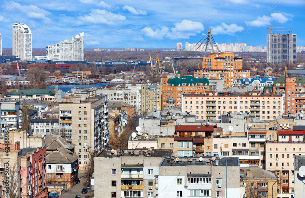 The cityscape of the streets of old Podil in Kyiv against the background of new residential buildings under construction on the horizon and the Northern Bridge over the Dnipro River.