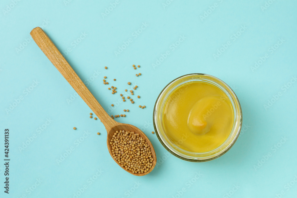 Jar with mustard and spoon with seeds on blue background Jar with mustard and spoon with seeds on blue background