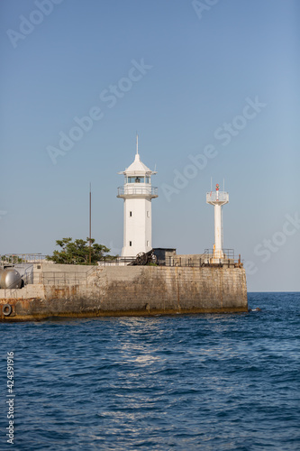 White lighthouse on the beach on a clear sunny day. There is a cannon nearby.