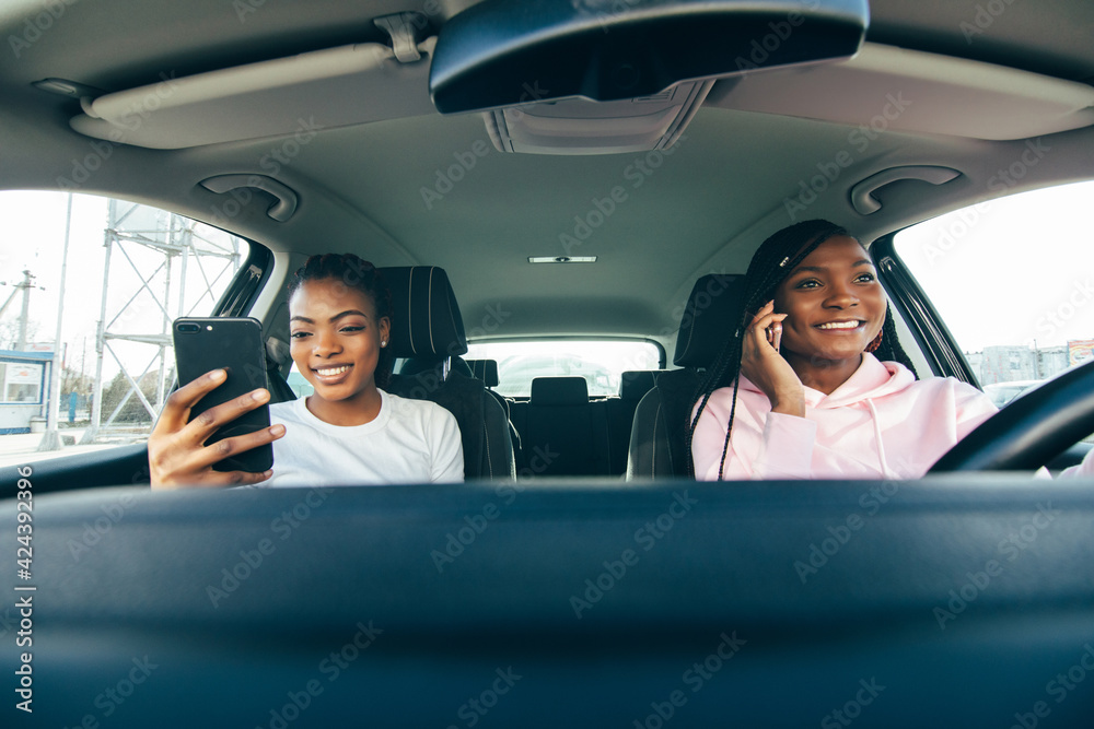 Two african woman talking on the phones in the car while driving car on the road