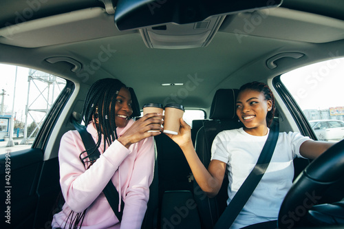 Happy african women friends with cup of coffee in car. Holiday trip of friends