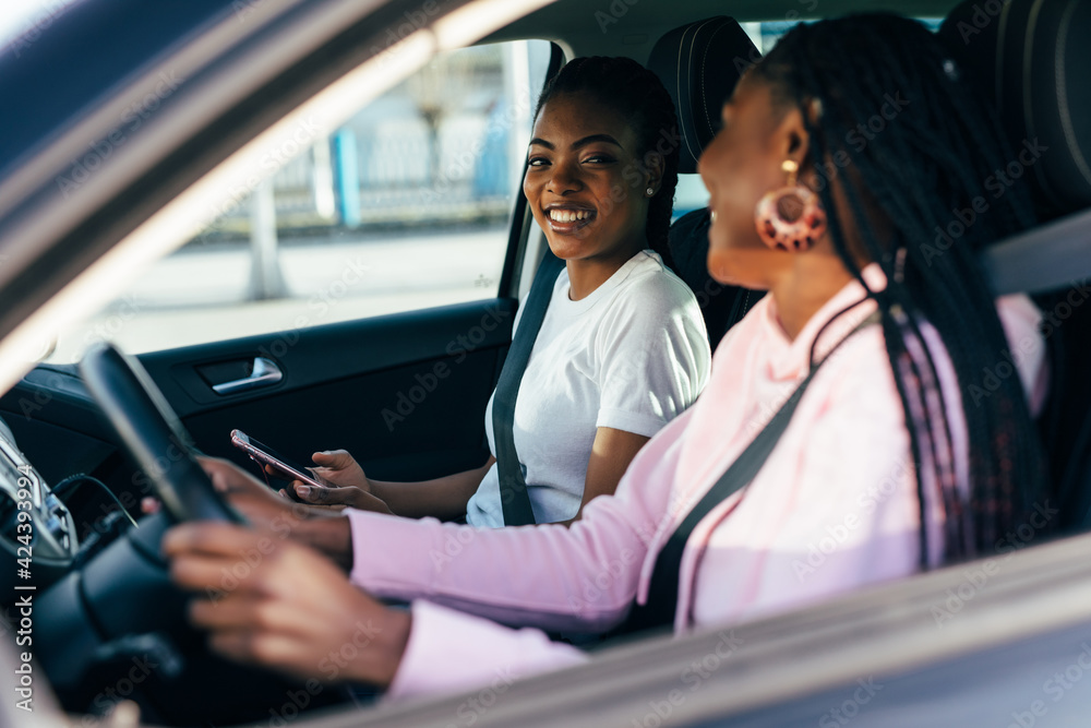 Two beautiful and pretty african women driving in car of their dream. Two women smiling because of successful purchase of automobile in car dealership. - obrazy, fototapety, plakaty 