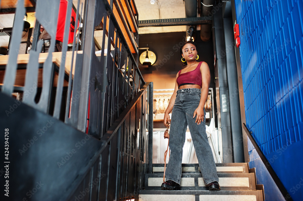 African woman in red marsala top and jeans posed indoor. African woman in red marsala top and jeans posed indoor.