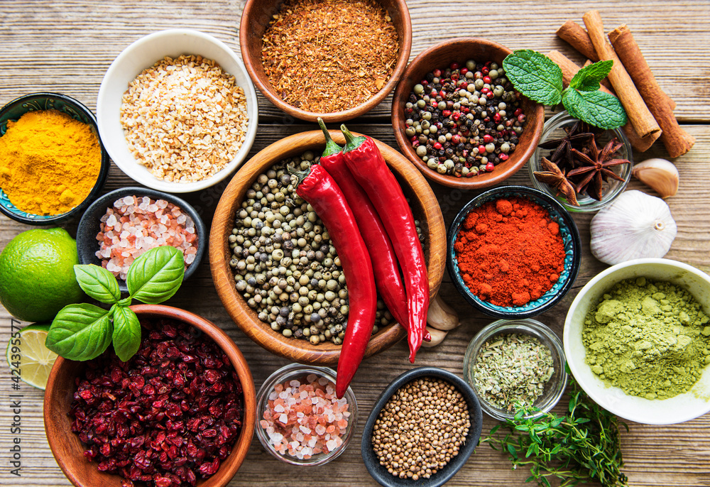 A selection of various colorful spices on a wooden table in bowls and spoons A selection of various colorful spices on a wooden table in bowls and spoons