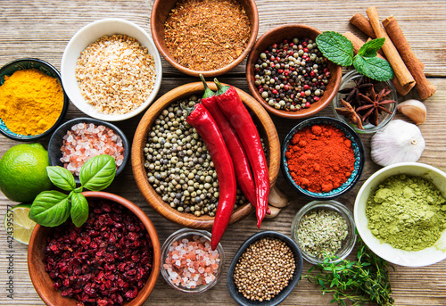 A selection of various colorful spices on a wooden table in bowls and spoons