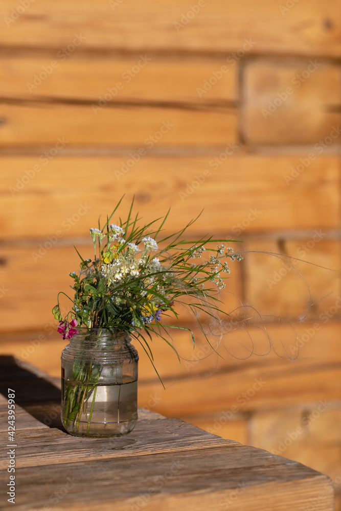 Modest bouquet of white and pink wildflowers with green twigs in glass jar is placed on wooden table in oudoor. Summer still life. Pleasant memories. Modest bouquet of white and pink wildflowers with green twigs in glass jar is placed on wooden table in oudoor. Summer still life. Pleasant memories.