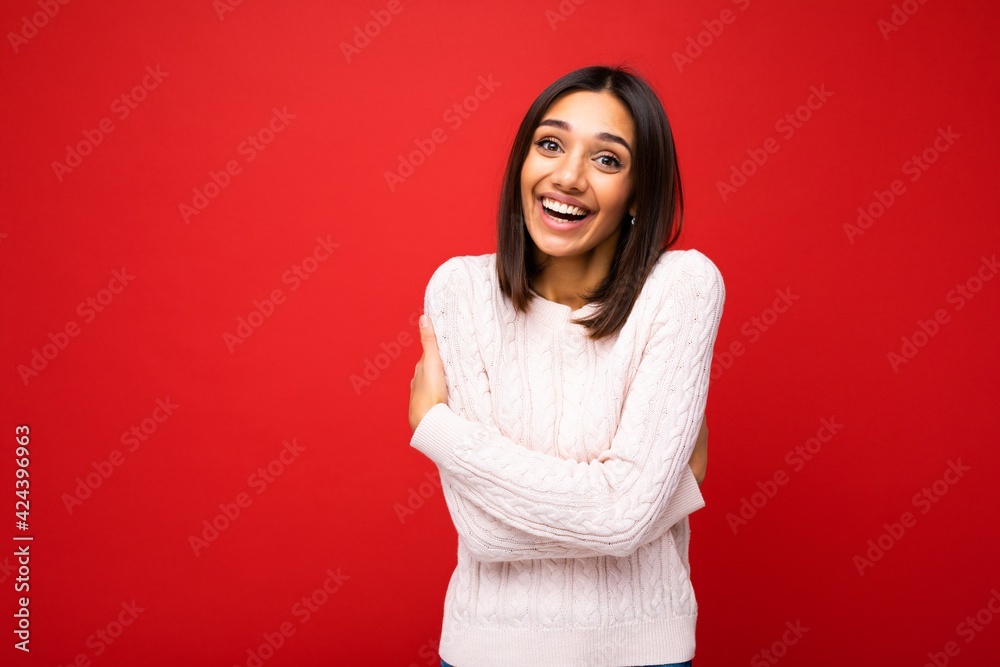 Photo of young beautiful happy smiling brunette woman wearing trendy light jersey . Sexy carefree female person posing isolated near red wall in studio with free space. Positive model with natural