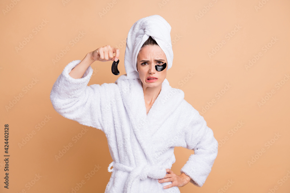 Portrait of pretty dissafisfied girl wear bathrobe ungly nourishing eye patches isolated over beige pastel color background Portrait of pretty dissafisfied girl wear bathrobe ungly nourishing eye patches isolated over beige pastel color background