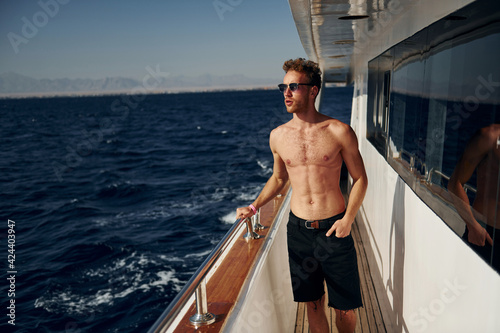 Warm weather. Young male tourist is on the yacht on the sea. Conception of vacation